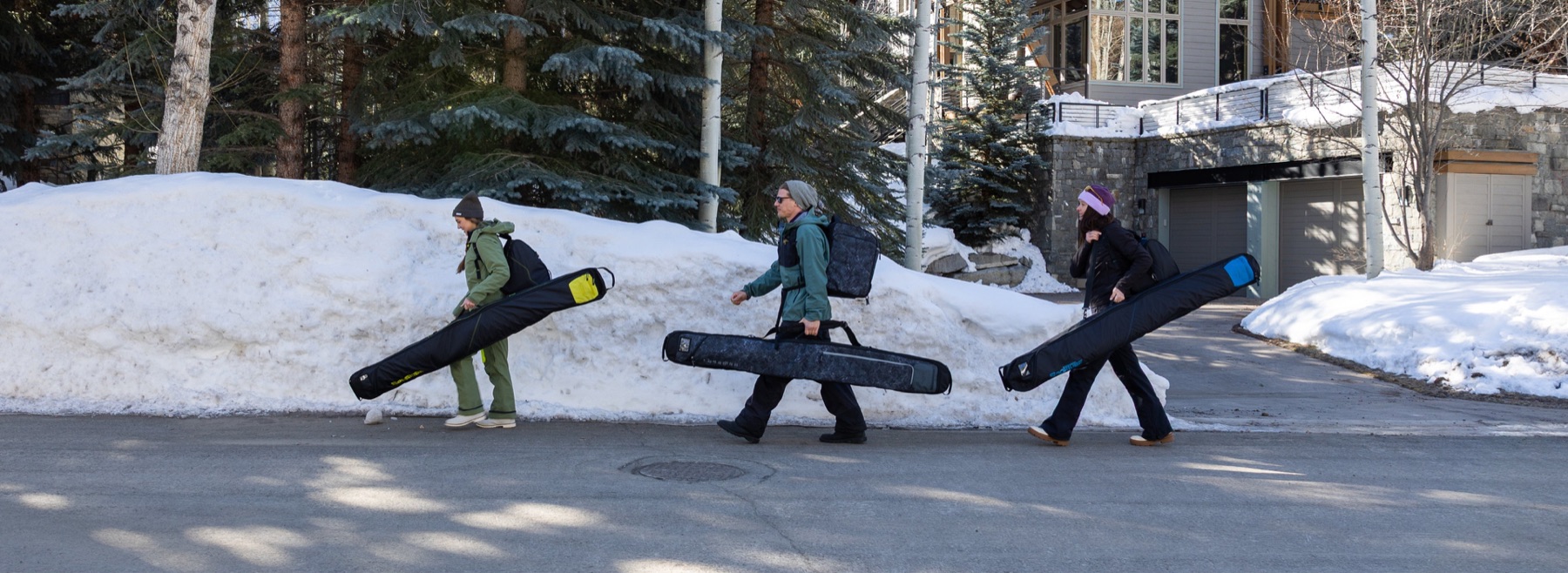 Three travelers carrying Sportube hard cases through Vail